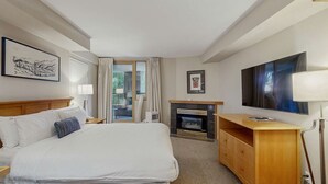 Una habitación de hotel con cama, televisión, chimenea y ventana con cortinas.