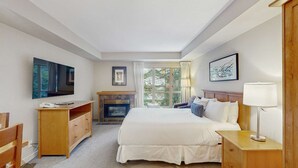 Una habitación de hotel con cama, televisión, chimenea, ventana con cortinas, lámpara de noche y escritorio con teléfono.