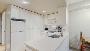 Una cocina compacta con armarios blancos, un microondas integrado, una estufa y un lavaplatos.