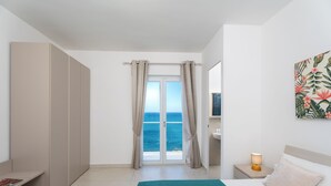 Un dormitorio con cama, mesita de noche, ventana con cortinas, vista al mar y armario.