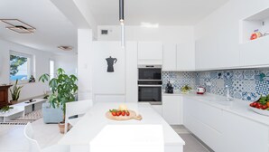 Una cocina moderna con armarios blancos, una isla central con tabla de cortar y verduras, y salpicadero con azulejos azules y blancos.