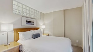 Habitación de hotel con una cama, dos mesitas de noche, una lámpara, un cuadro en la pared y una ventana con cortinas.