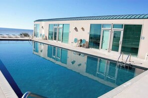 Ein Schwimmbecken mit Liegestühlen und ein Gebäude mit großen Fenstern.