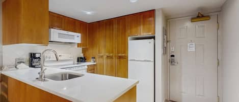 A kitchen with wooden cabinets, a white countertop, a built-in microwave, a refrigerator, and a sink.