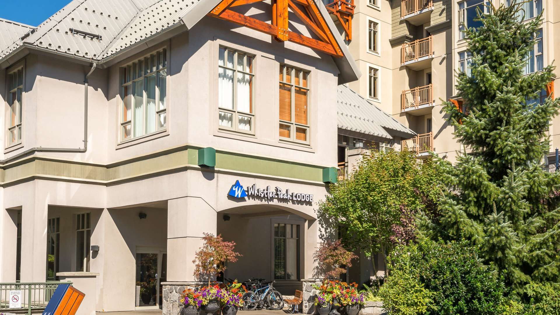 Un edificio con un letrero que dice "Whistler Peak Lodge". Presenta un estilo arquitectónico moderno con un alero pronunciado y amplias ventanas.