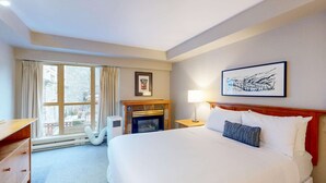 A hotel room with a bed, a fireplace, a window with curtains, a framed picture on the wall, and a lamp on the nightstand. - Whistler - Whistler Peak Lodge 315 (Whistler)
