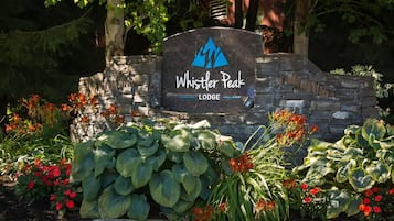 Señal de Whistler Peak Lodge rodeada de vegetación exuberante y plantas en flor.
