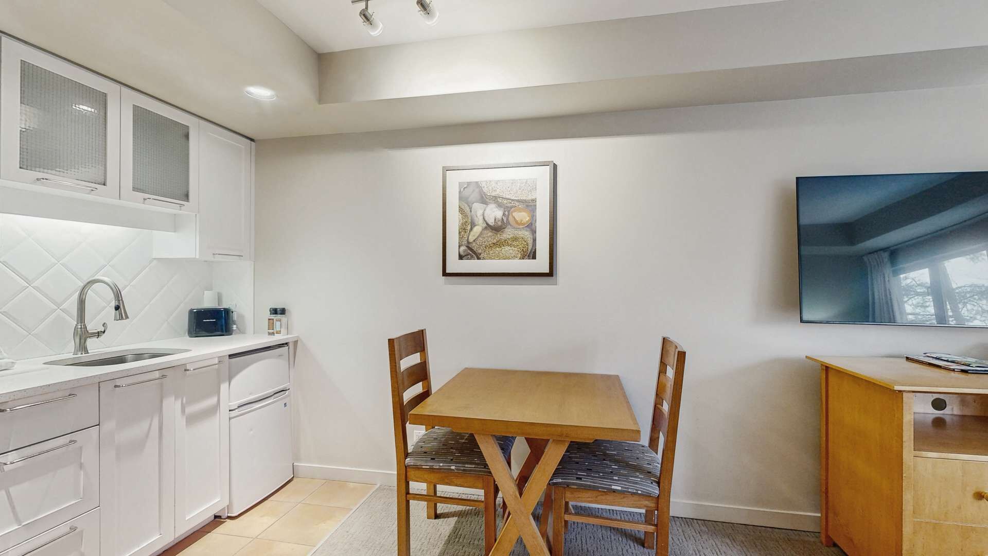Een moderne keuken met witte kasten, een eettafel met stoelen, een kunstwerk in een lijst aan de muur en een groot raam.