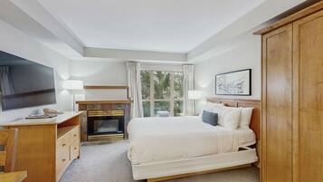Un dormitorio con cama, televisión, chimenea, ventana con cortinas y un armario de madera.