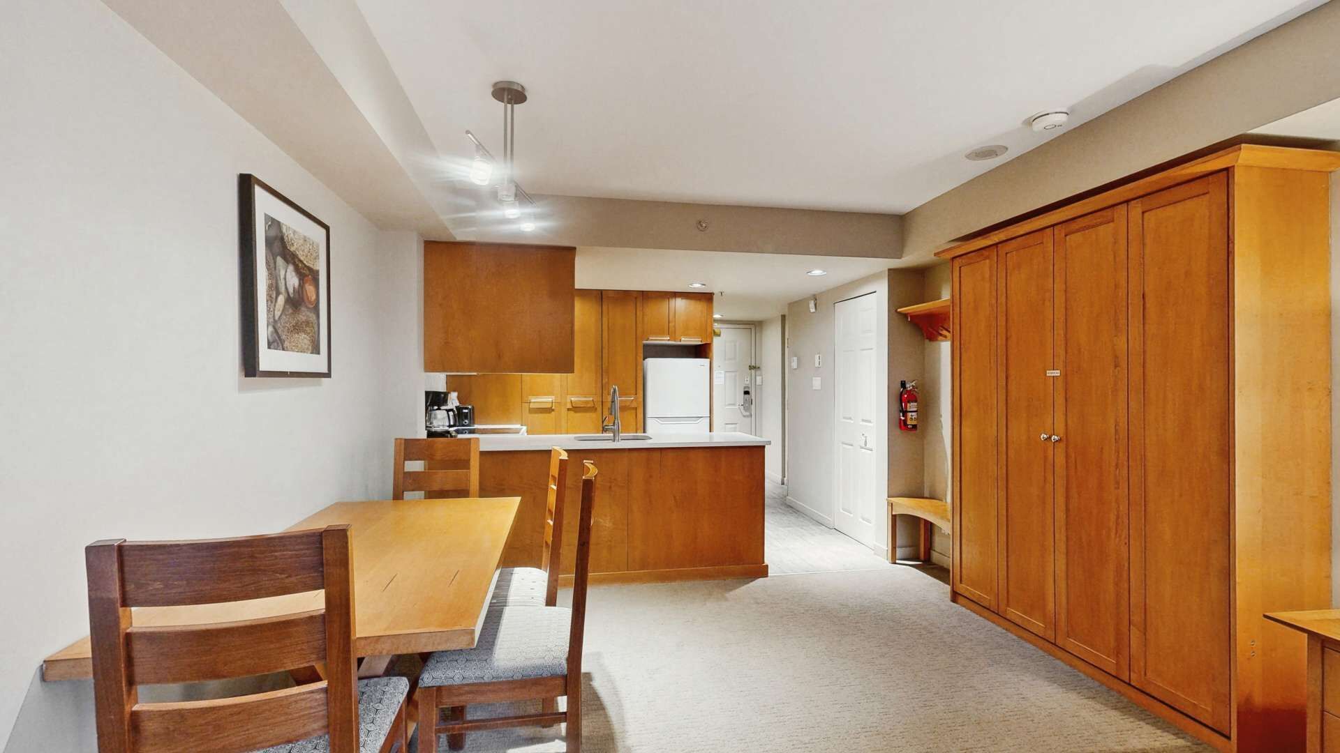 A modern kitchen with wooden cabinets, a dining table with chairs, and a large wooden wardrobe.