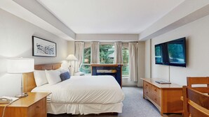 A hotel room with a bed, bedside tables, a TV, a fireplace, and a window with curtains. - Whistler - Whistler Peak Lodge 3303 (Whistler)