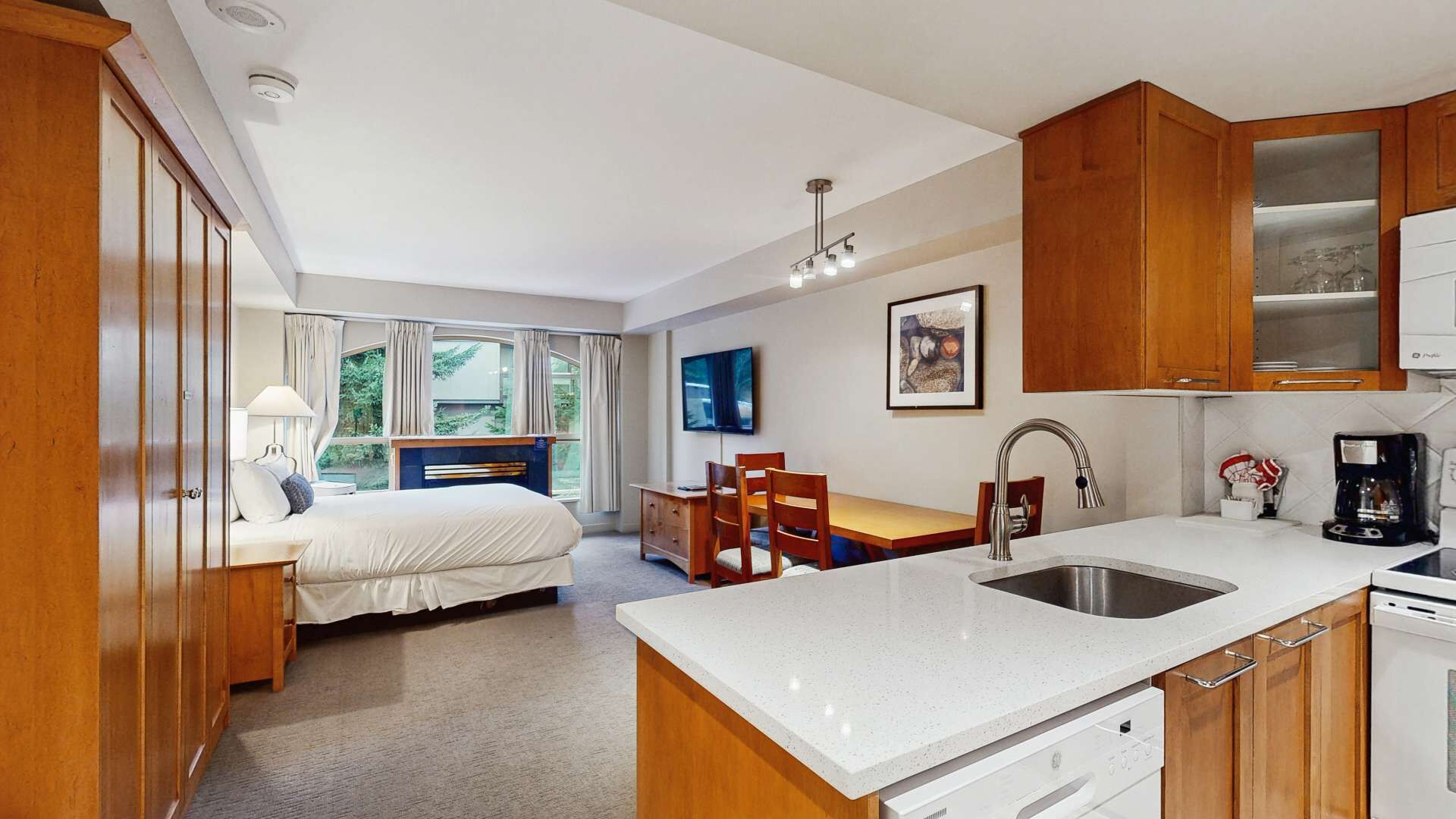 Une chambre d’hôtel de taille réduite comprenant un lit, un bureau, un coin repas et une kitchenette.
