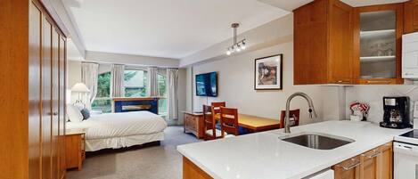 Une chambre d’hôtel de taille réduite comprenant un lit, un bureau, un coin repas et une kitchenette.