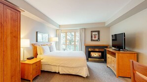 Habitación de hotel con cama, mesita de noche, lámpara, televisión, chimenea y ventana con vista a árboles.