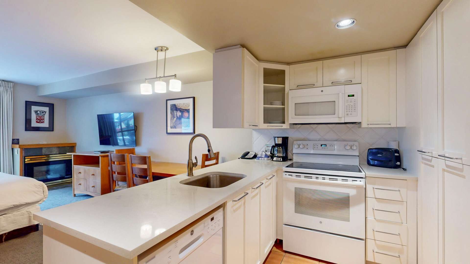 A compact hotel kitchen with white cabinetry, a built-in microwave, a stove, and a sink.