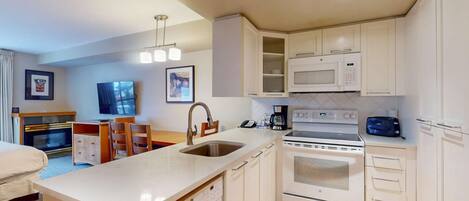 A compact hotel kitchen with white cabinetry, a built-in microwave, a stove, and a sink.