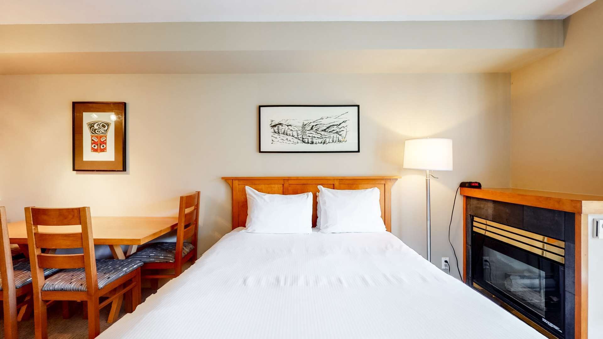 Een hotelkamer met een bed, een bureau met stoelen, een lijst, een lamp en een open haard.