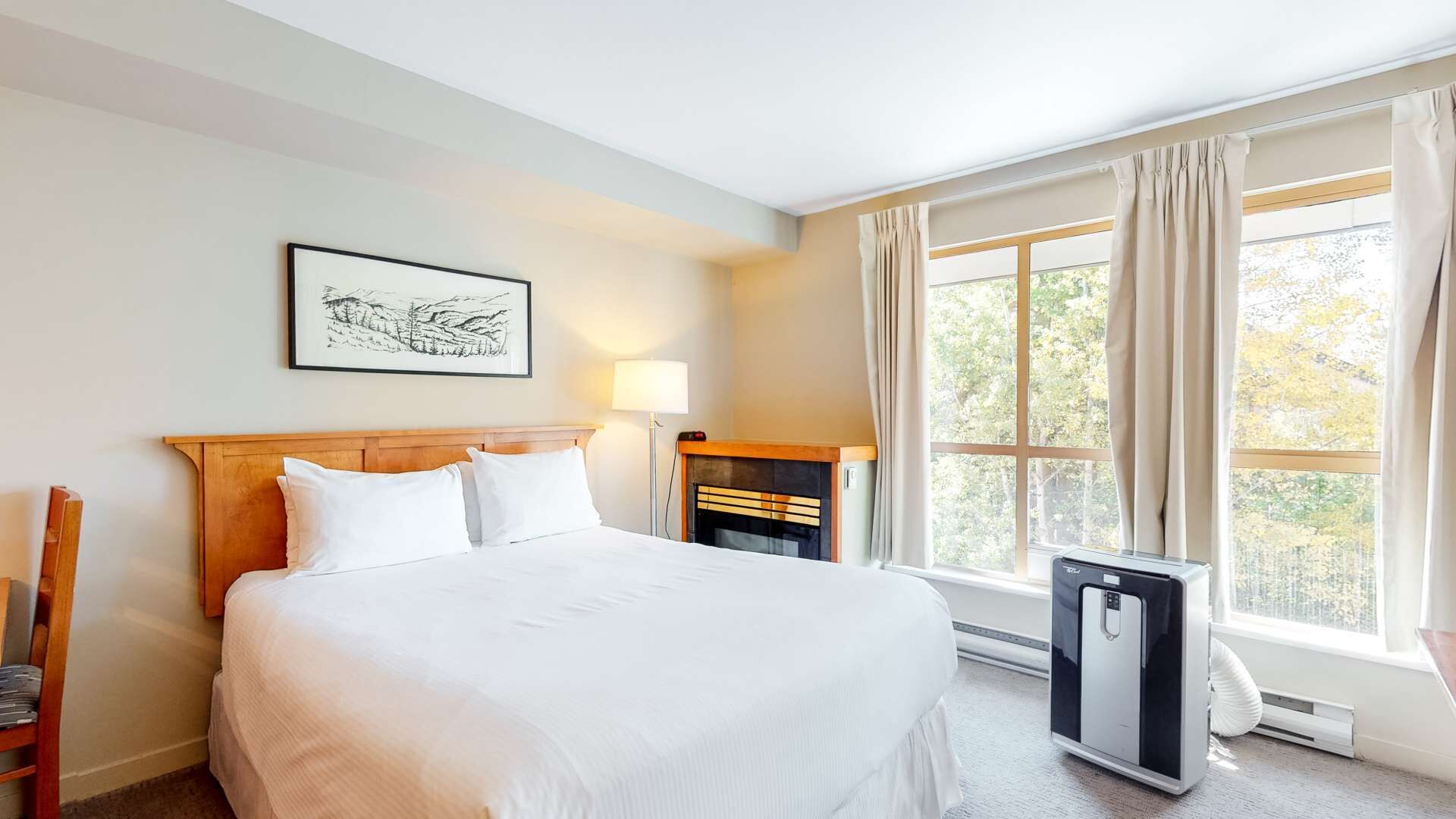 A hotel room with a large bed, a bedside table with a lamp, a small heater, and a window with curtains.