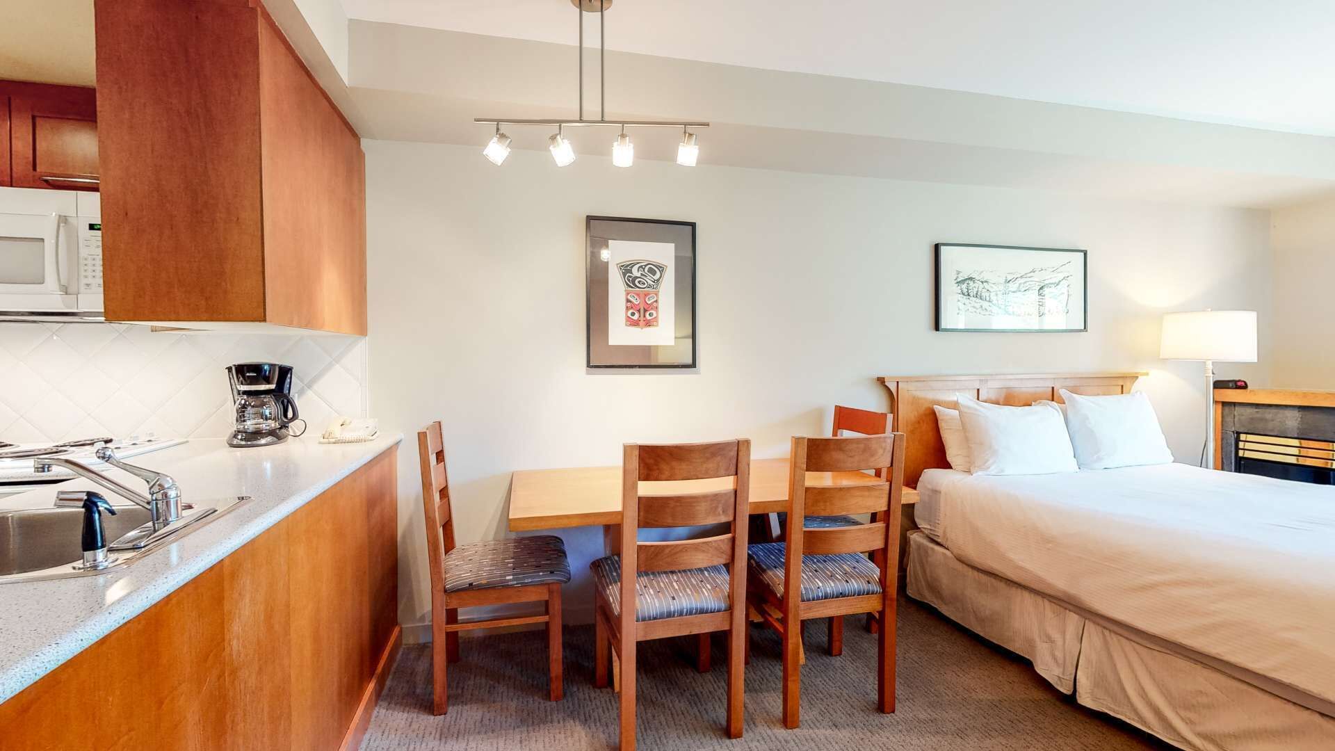 A hotel room with a kitchenette, a dining area with a table and chairs, a bed, and two framed pictures on the wall.