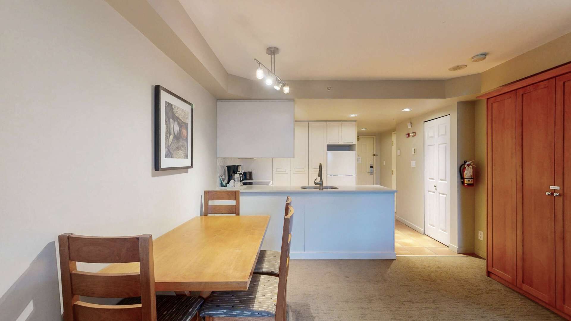 Una cocina compacta con gabinetes blancos, una isla central y un comedor con mesa y sillas de madera.