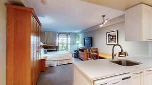 Habitación de hotel con cama, escritorio, silla, mesa de comedor y cocina equipada con lavaplatos y fregadero.