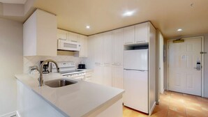 Una cocina moderna con armarios blancos, un lavamanos de acero inoxidable, un microondas, una estufa y un refrigerador.