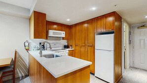 A compact kitchen with wooden cabinets, a white countertop, a sink, a microwave, and a refrigerator. - Whistler - Whistler Peak Lodge 414 (Whistler)