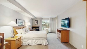 Een hotelkamer met een bed, nachtlampjes, een televisie, een bureau en een raam met gordijnen.