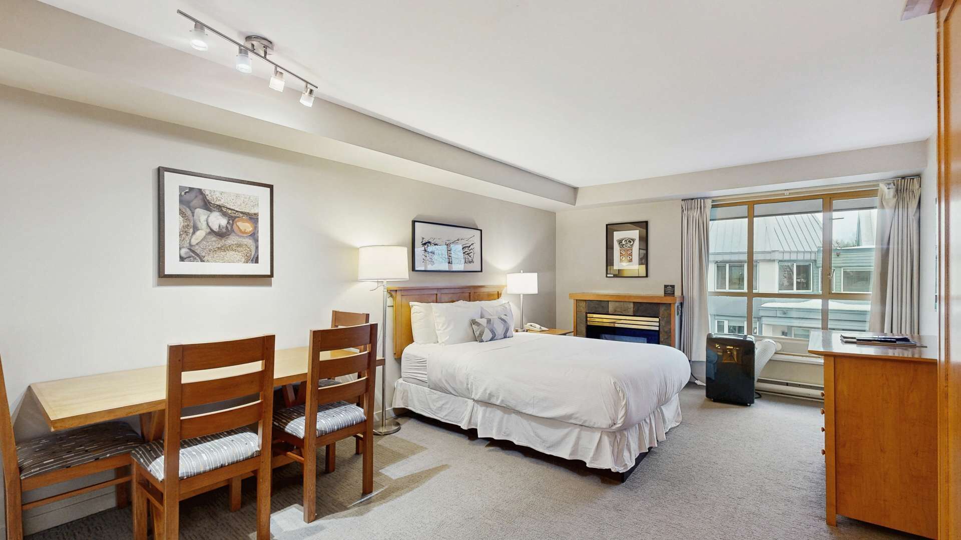 A hotel room with a bed, desk, chairs, and a window with a view.