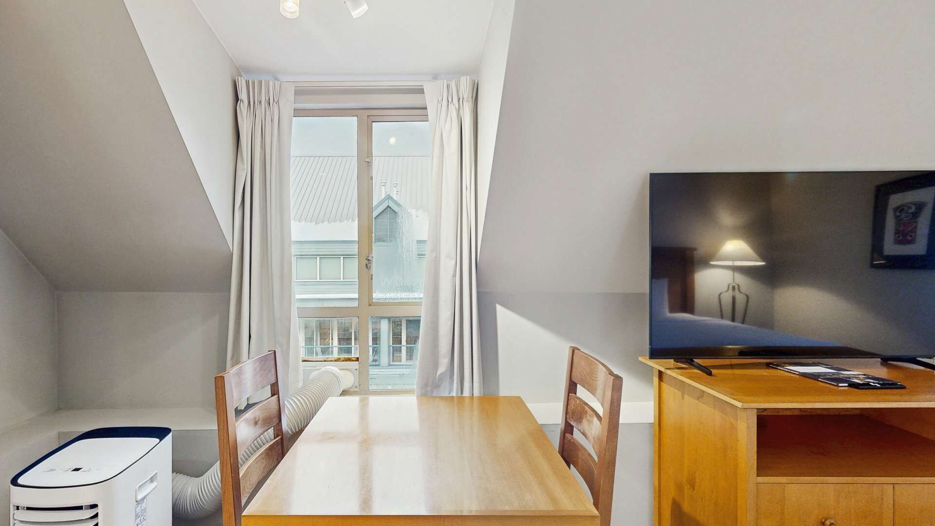 Ein Zimmer mit Esstisch, Stühlen, Fernseher und einem kleinen Schreibtisch mit Lampe.