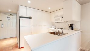 Cocina moderna con armarios blancos, un lavamanos de acero inoxidable, un microondas y una cafetera.