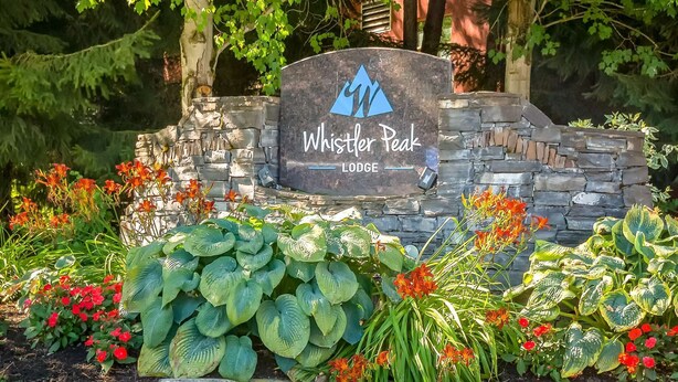 A stone sign with a logo and the text 'Whistler Peak Lodge' surrounded by lush greenery and flowers. - Whistler - Whistler Peak Lodge 418 (Whistler)