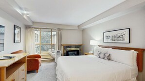 A hotel room with a bed, desk, chair, fireplace, and a window with curtains. - Whistler - Whistler Peak Lodge 428 (Whistler)