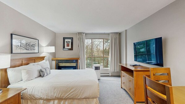 Ein Hotelzimmer mit Bett, Schreibtisch, Stuhl, Fernseher, Kamin und einem Fenster mit Vorhängen.