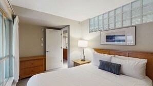 Een hotelkamer met een bed, nachtkastje, lamp en uitzicht door een raam.