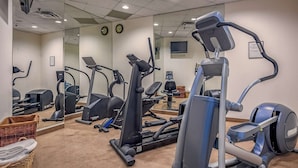 Ein Fitnessraum mit verschiedenen Cardiogeräten, einer Spiegelwand und einer Uhr.