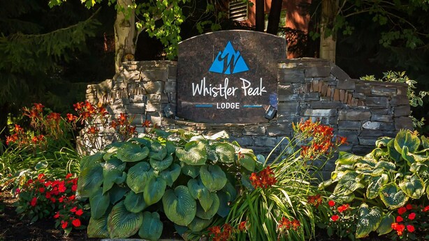 A sign for Whistler Peak Lodge surrounded by lush greenery and flowering plants. - Whistler - Whistler Peak Lodge 504 (Whistler)