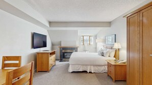 A bedroom with a TV, a fireplace, a bed, a desk, and a wardrobe. - Whistler - Whistler Peak Lodge 504 (Whistler)