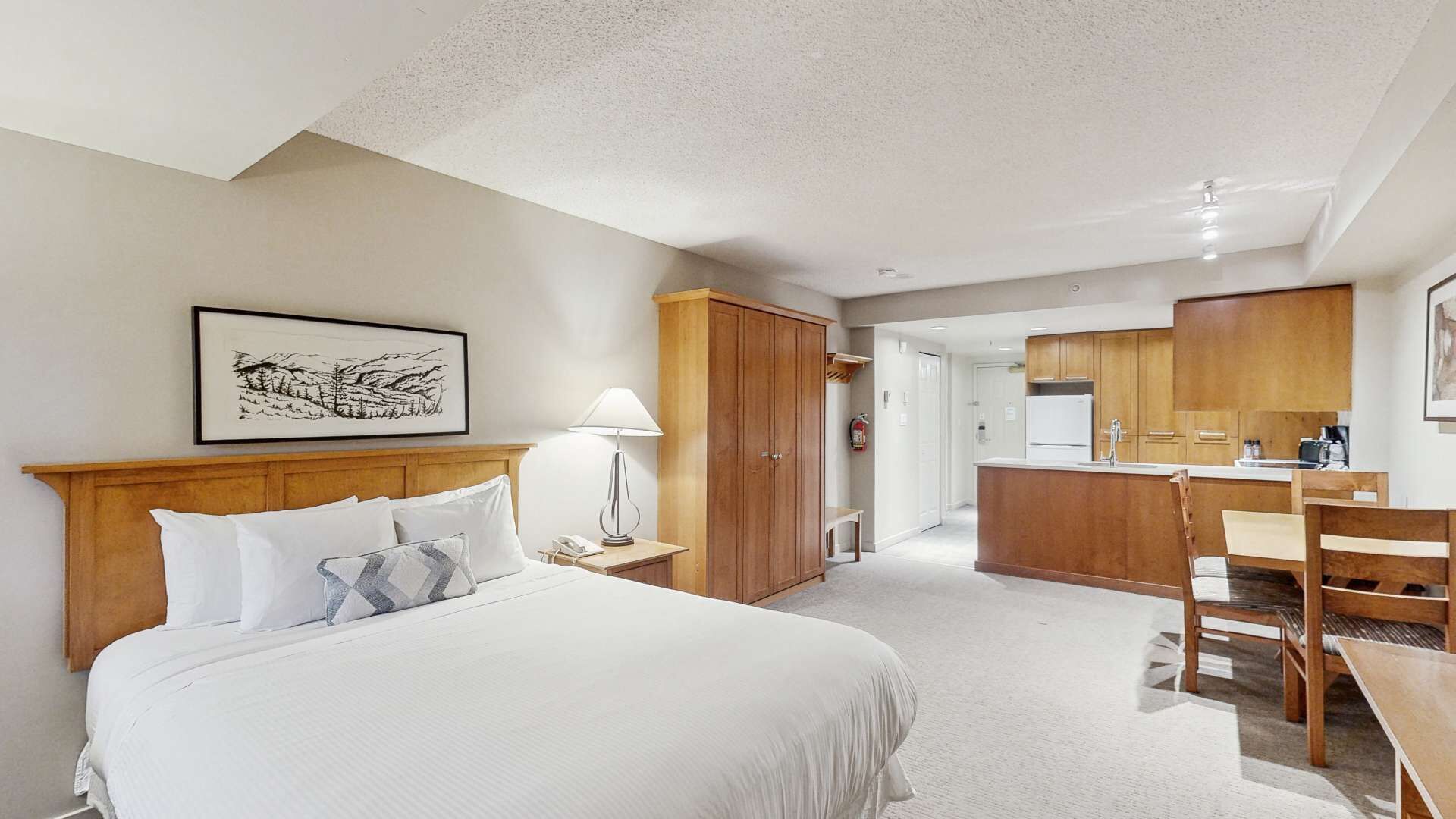 Een hotelkamer met een bed, nachtkastje, lamp, garderobe en een kitchenette.