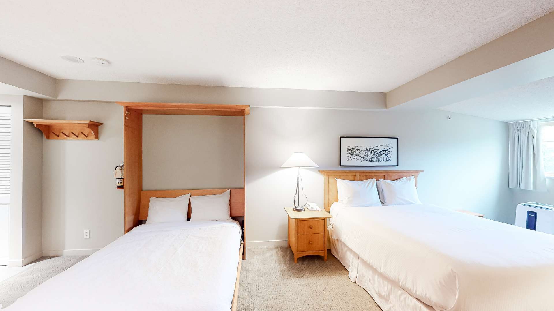 A hotel room with two beds, a wooden headboard, a nightstand with a lamp, a framed picture on the wall, and a window with curtains.