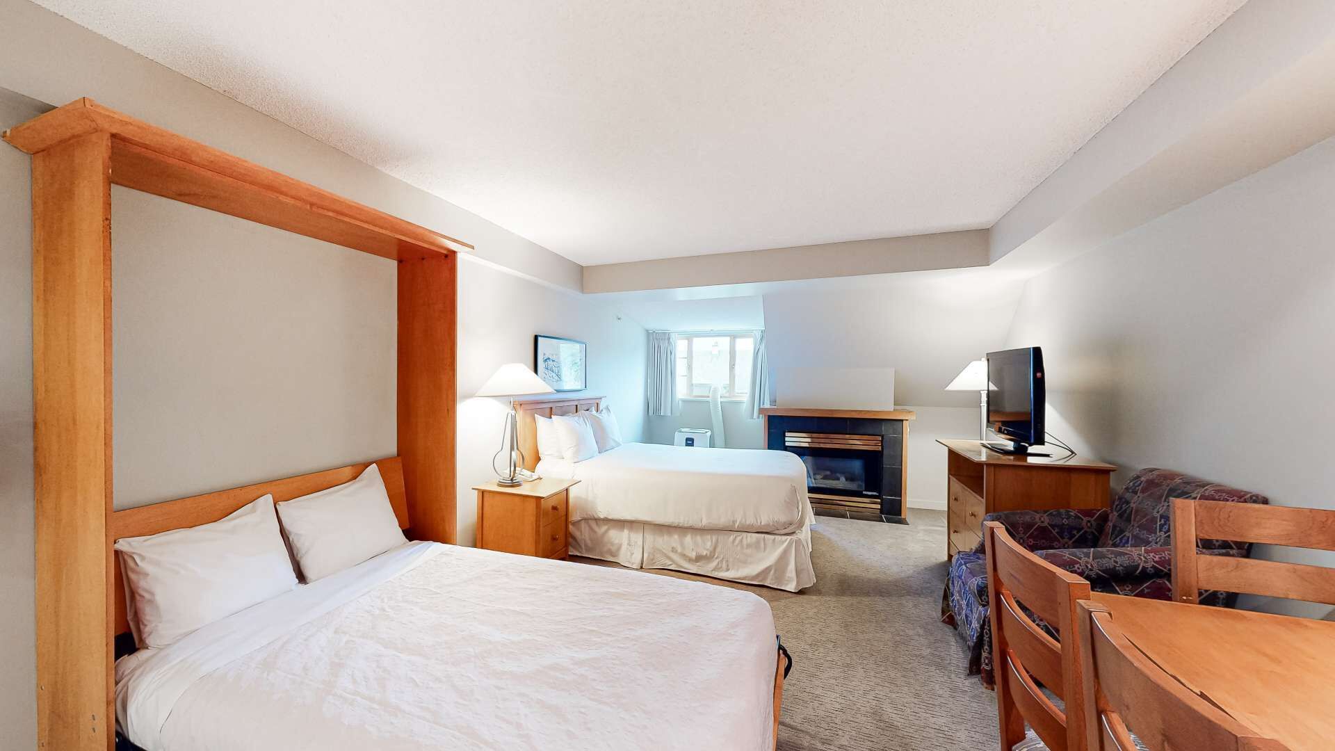Habitación de hotel con dos camas, televisión, escritorio y chimenea.