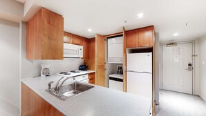 Una cocina moderna con armarios de madera, un lavamanos de acero inoxidable, una encimera blanca, un microondas, una estufa y un refrigerador.