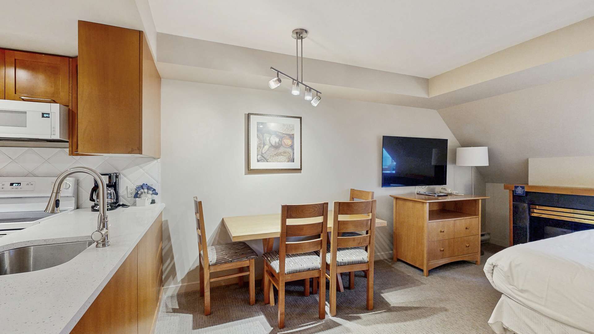 Habitación de hotel compacta con kitchenette, comedor con sillas, escritorio con silla, televisor y cama.