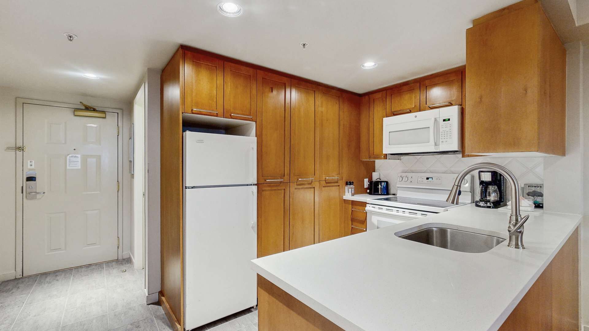 A compact kitchen with wooden cabinets, a white refrigerator, a microwave, an oven, and a sink.