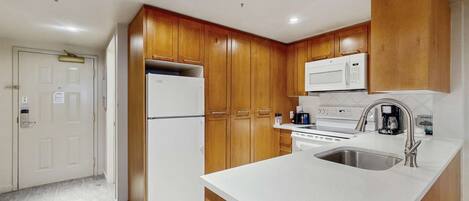 A compact kitchen with wooden cabinets, a white refrigerator, a microwave, an oven, and a sink.