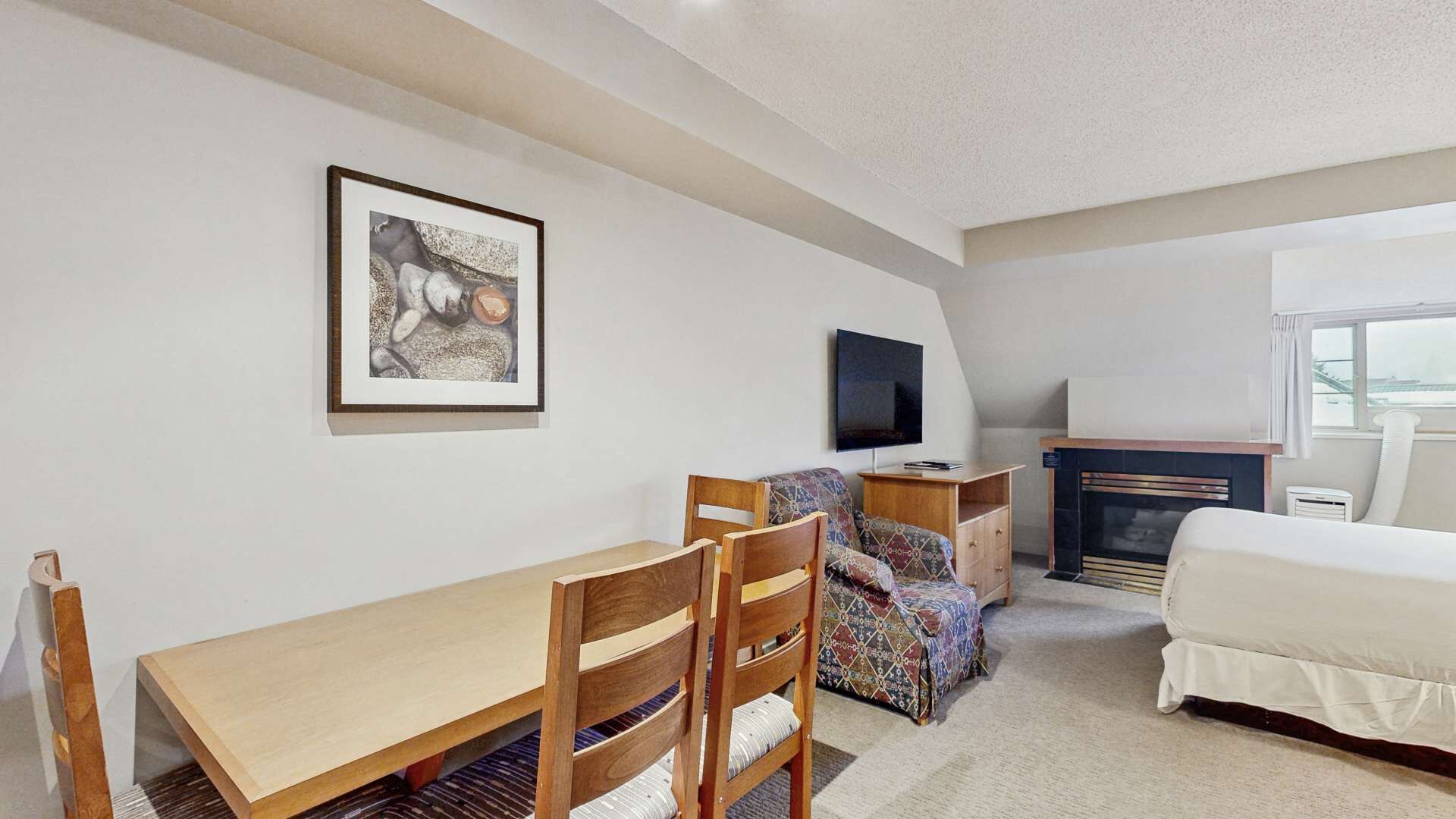 A bedroom with a bed, a desk, a chair, a television, and a fireplace.