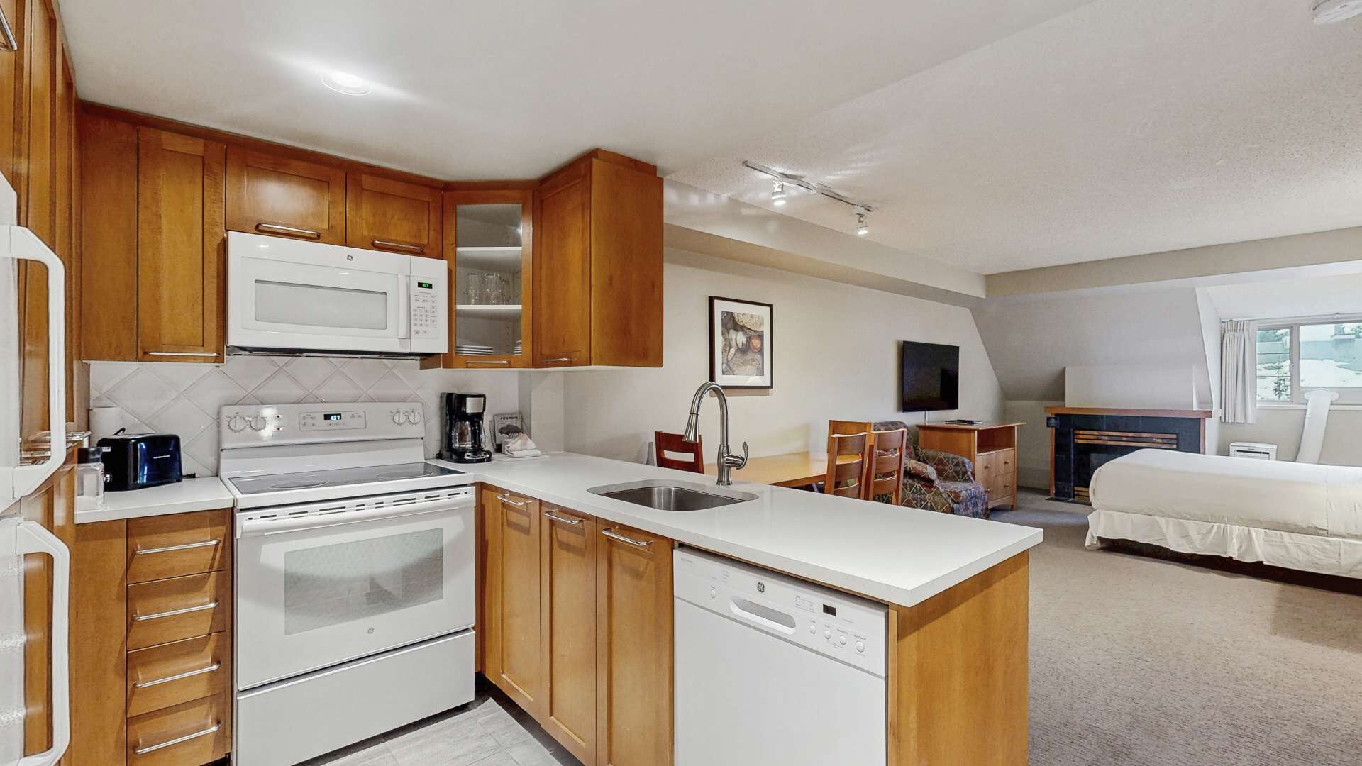 A compact kitchen with wooden cabinets, a microwave, a stove, and a dishwasher.