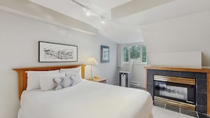 A bedroom with a bed, a nightstand, a lamp, a fireplace, and a window. - Whistler - Whistler Peak Lodge 502 (Whistler)