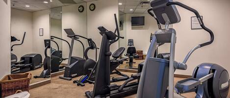 A gym with various exercise machines, a clock, and a television on the wall.