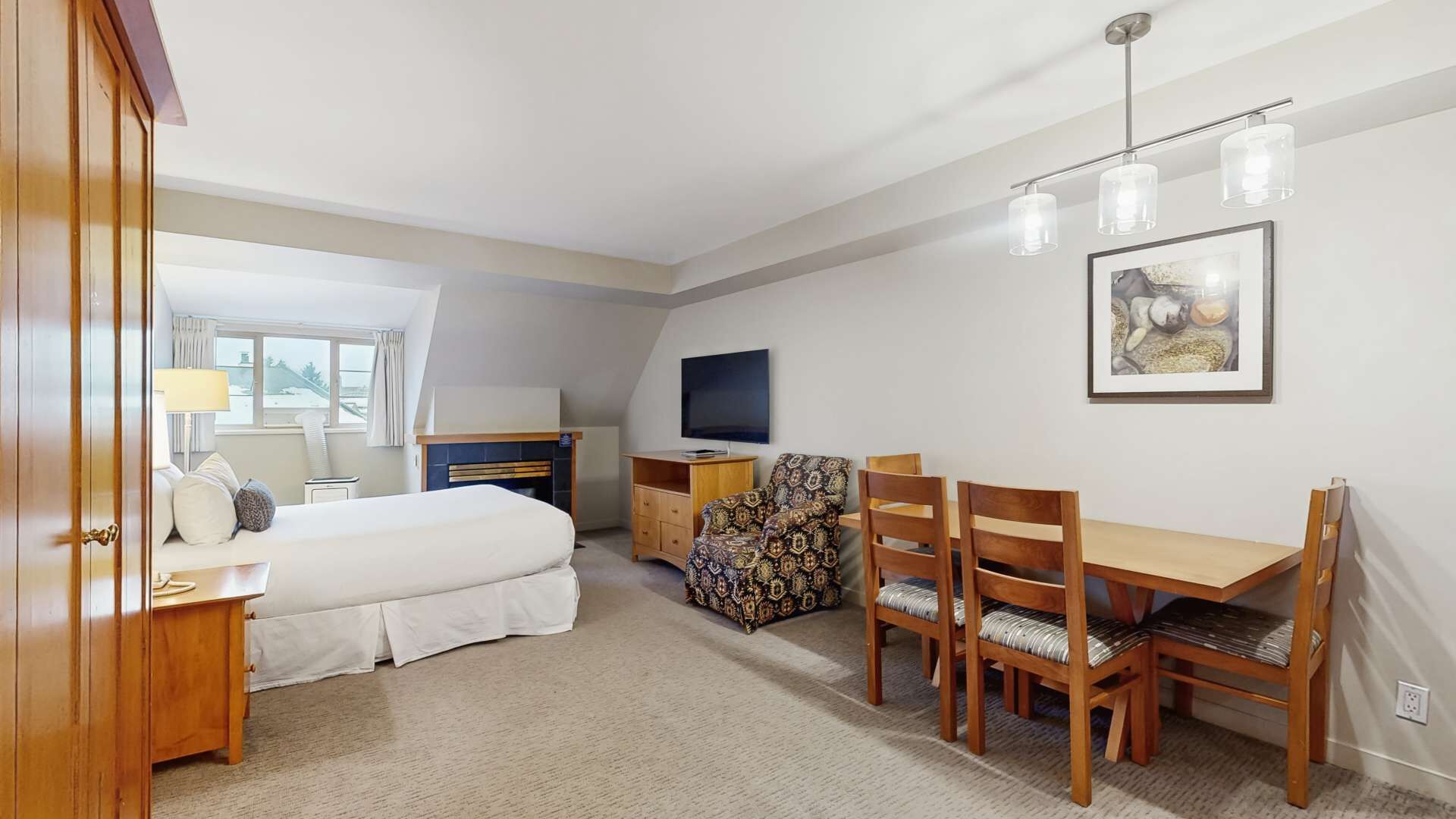 A hotel room with a bed, a desk, a TV, a dining table with chairs, and a fireplace.